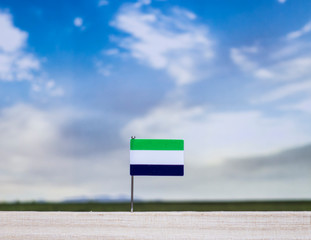 Flag of Sierra Leone with vast meadow and blue sky behind it.