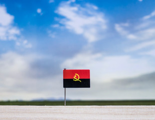 Flag of Angola with vast meadow and blue sky behind it.