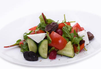 Fresh salad plate with mixed greens (arugula, mesclun, mache) with tomatoes, cucumbers and slices of cheese.  Isolated on white on a white plate. Healthy food.