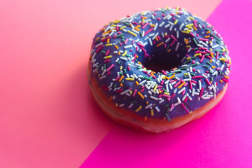 sweet Donut with icing and color dusting, on a pink background, side view