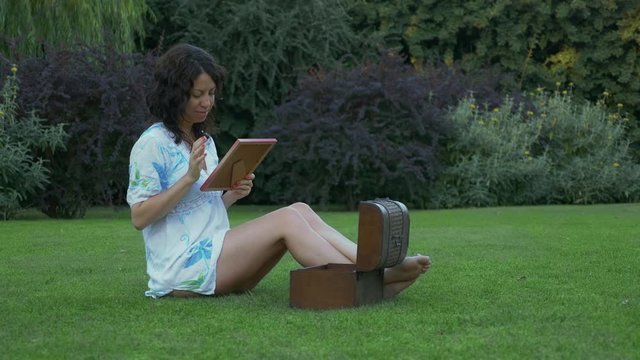 Woman opening a chest full of pictures in a garden