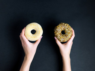 Female hands holding tasty donuts on dark background, top view, place for text