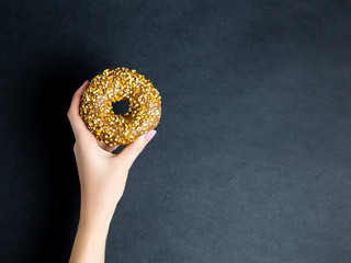 Woman hand hold sweet chocolate donut on black background, top view, place for text, copy space