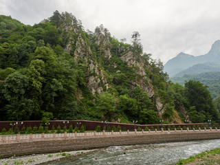 Pedestrian embankment of a mountain river in front of cliffs.