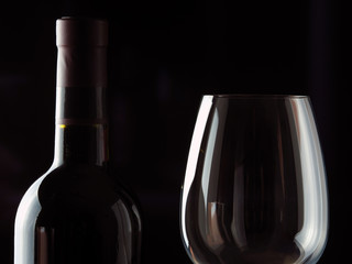 A bottle of red wine with a beautiful wine glass against a dark background