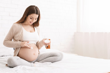 Pregnant woman applying stretch mark cream to belly