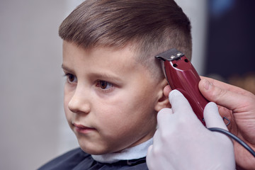 ber making a haircut to a cute European boy using cutting machine.