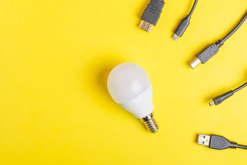 White light bulb in the middle surrounded by USB wires. Minimal concept on yellow background