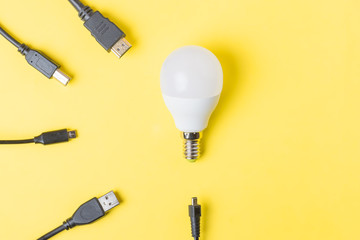 White light bulb in the middle surrounded by USB wires. Minimal concept on yellow background