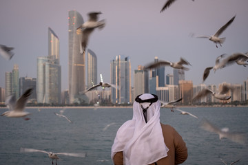 Local emirati enjoying the view of hovering seagulls against abu dhabi seascape, Abu Dhabi, UAE