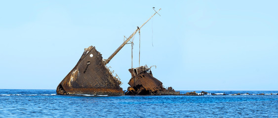 sea view with abandoned shipwreck near coast with ocean waves and blue sky