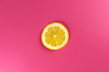 A single slice of lemon isolated on a pink background, illuminated by a soft light.