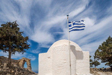 The apse of a typical Greek church with the flag in the wind among the ruins of the medieval castle...