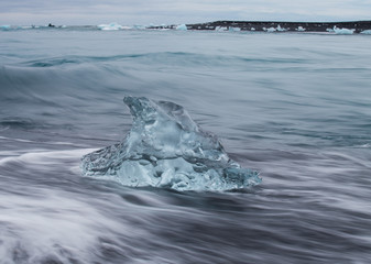 Amazing transparent blue iceberg pieces on Diamond beach with black sand near Jokulsarlon lagoon, Iceland. Ice calving. Water long exposure.