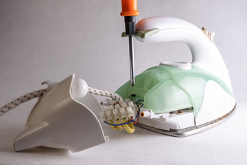 Household appliance repair concept. Green broken iron. The electrician disassembles the appliance with an orange screwdriver.