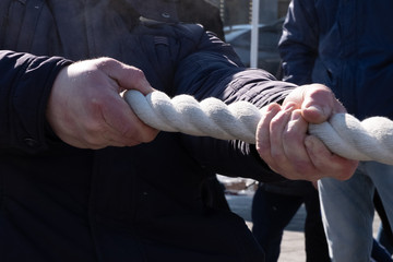Male hands holding a rope. Tug of war. Close-up. Folk games and fun. Autumn or spring.