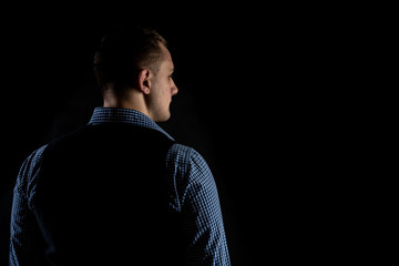 A man stands with his back to the camera and looks away. A man thinks and decides. Black background