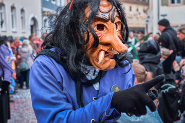 Witch in violet robe points with his finger. Street Carnival in Southern Germany - Black Forest.