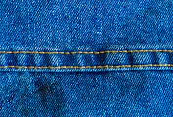 Denim or rough cotton fabric or jeans material with the stitched seam for the textile textured background of pale blue color. Macro shot