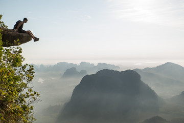 Dizziness concept: person sitting on the end of a mountain cliff looking down at the jump