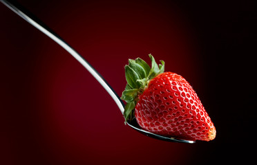 Strawberry in spoon on a dark background.