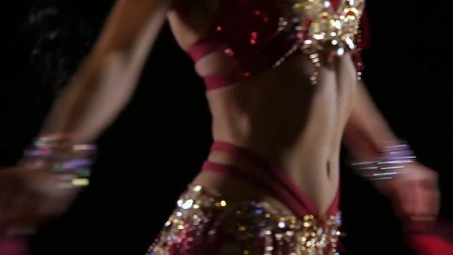 Shiny slim torso of a young girl female belly dancer. Black background. Slow motion. Close up