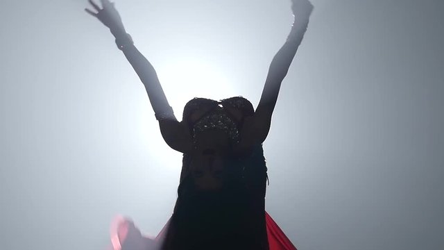 Woman standing back in costume with dancing belly dance . Smoke background. Slow motion. Sihouette