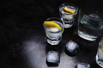 Vodka. Shots, glasses with vodka and lemon with ice .Dark stone background.
