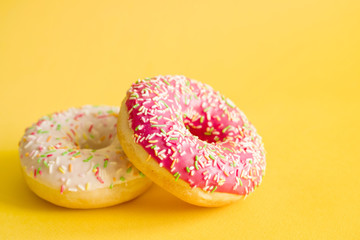Two colorful donuts on yellow background, closeup