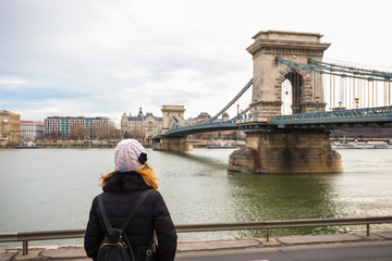 Young woman is looking at the Chain bridge from Danube riverbank by the road in Budapest, Hungary.