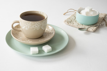 romantic breakfast scene with cup and saucer, tea, mint green bowl with sugar cubes