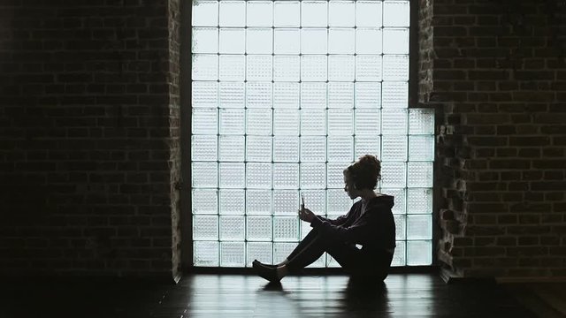 Girl sitting on the floor in a dark room and listening to music on her phone 