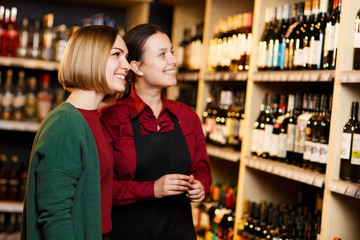 Image of two smiling women on blurred background of shelves with bottles of wine
