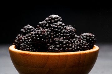 Photo of blackberry in wooden cup on empty black background.
