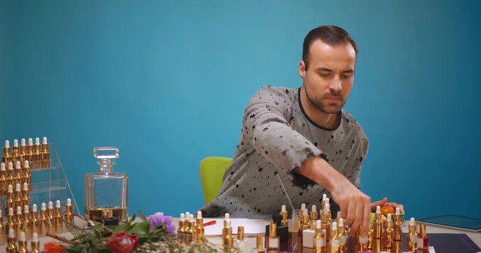 Male perfumer choosing oils and adding them into alcohol mixture