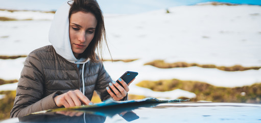 girl hold in hands mobile phone looking on map, relax tourist travels by auto car, people planning trip in snow mountain, hipster enjoy winter nature, journey landscape trip, lifestyle holiday concept