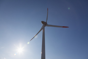wind turbine with sun flare blue sky background view from below