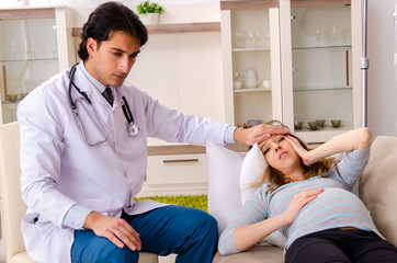 Obraz premium Young handsome doctor visiting pregnant woman at home