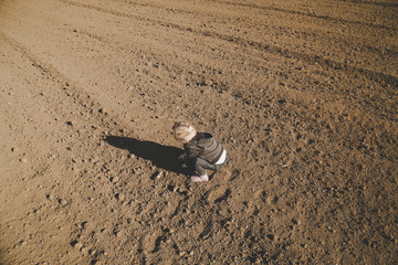 Cute baby girl playing with dirt on the flat plot agricultural land