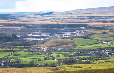 A massive rock quarry is seen from a distance in the Peak District, England.