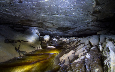 A dark cave with a stream flowing through it is illuminated by flashlight. Peak District, England.