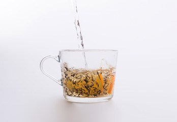 Water pouring into glass cup with tea and slices of orange isolated on white