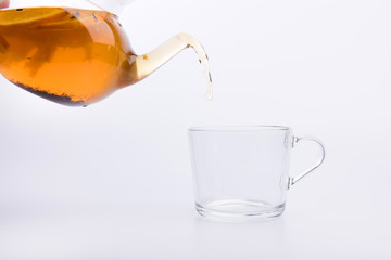 Glass teapot pouring tea into cup isolated on white background