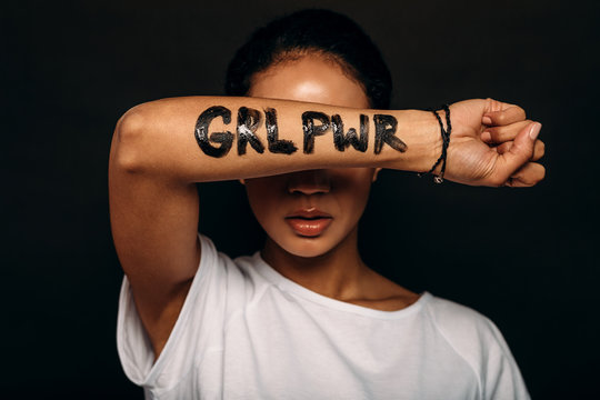 Woman with letters "GRL PWR" written on her hand. Portrait of a woman with arm covering a part of her face. - Powered by Adobe