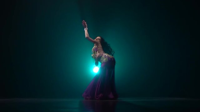 Traditional oriental belly dancer girl dancing on smoke background in dark scene. Slow motion