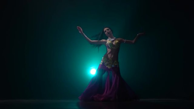 Traditional oriental belly dancer girl dancing on smoke background in dark scene. Slow motion