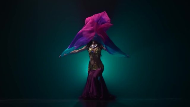 Girl with a veil in her hands dancing belly dance in dark studio. Smoke background. Slow motion