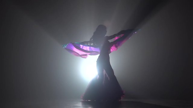 Exotic belly dancer woman continue dance uses fans. Sihouette . Black smoke background. Slow motion