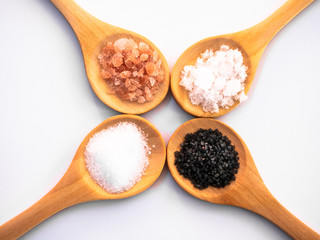 Wooden spoons with himalayan salt, black hawaii salt, common salt and salt flakes on a white background