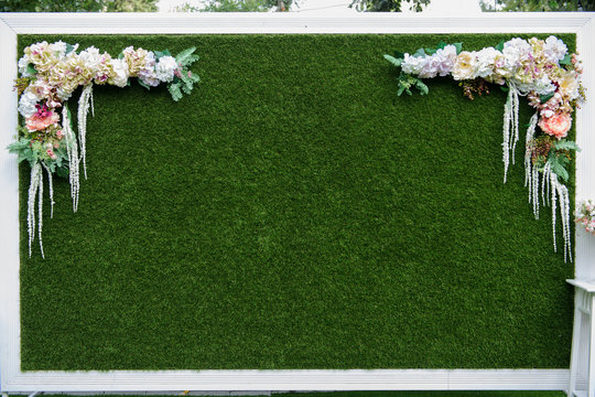 close up photo of a artificial grass wedding backdrop in a white frame decorated with flowers